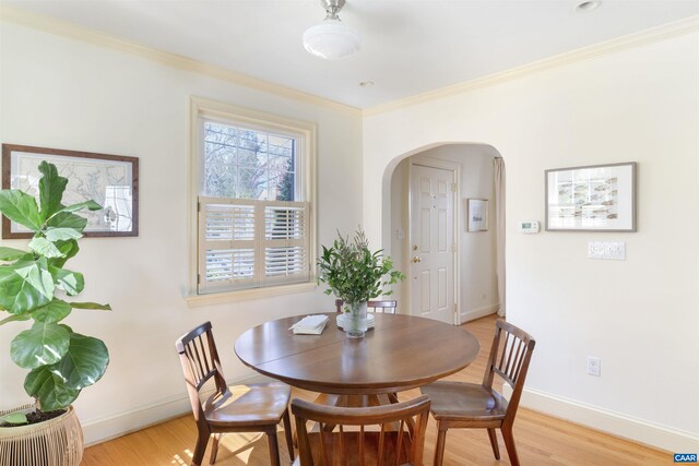 dining space featuring light wood-type flooring, arched walkways, baseboards, and ornamental molding