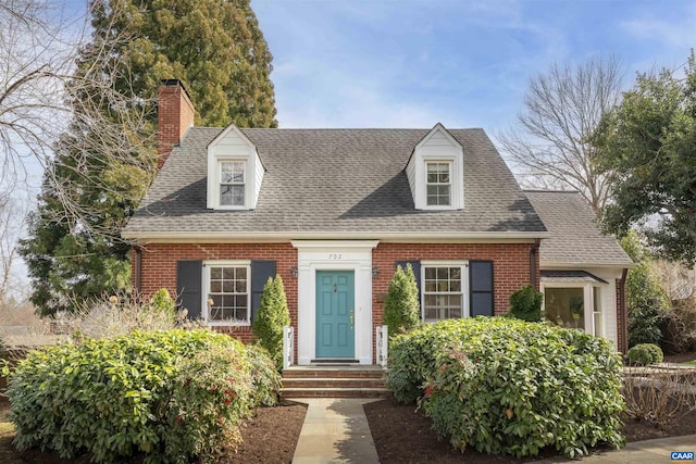 new england style home with brick siding, a chimney, and a shingled roof