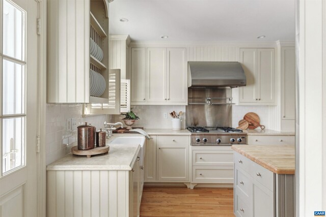 kitchen featuring light countertops, light wood-style flooring, exhaust hood, stainless steel gas stovetop, and a sink