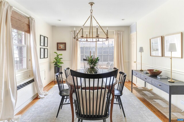 dining area featuring wood finished floors, radiator heating unit, wainscoting, a decorative wall, and a notable chandelier