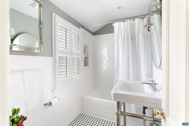 bathroom featuring tile patterned floors, shower / bath combo, a sink, tile walls, and lofted ceiling