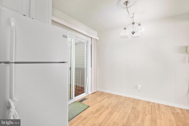 unfurnished dining area featuring an inviting chandelier and light hardwood / wood-style flooring