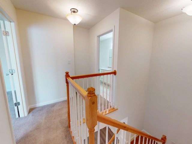 hallway with carpet floors, baseboards, and an upstairs landing
