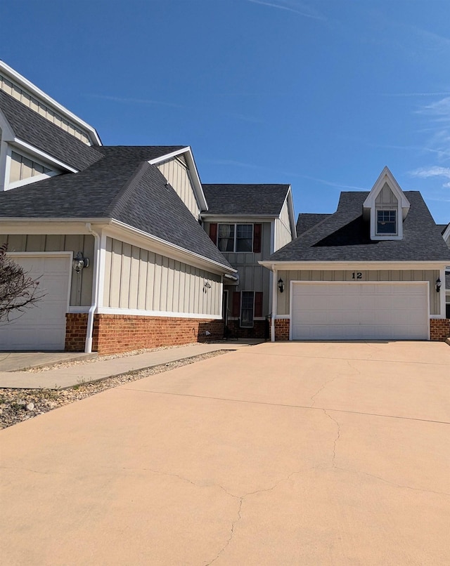 view of front of property featuring board and batten siding, brick siding, concrete driveway, and roof with shingles