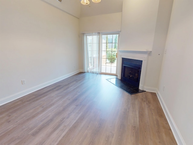 unfurnished living room with baseboards, a towering ceiling, wood finished floors, and a fireplace