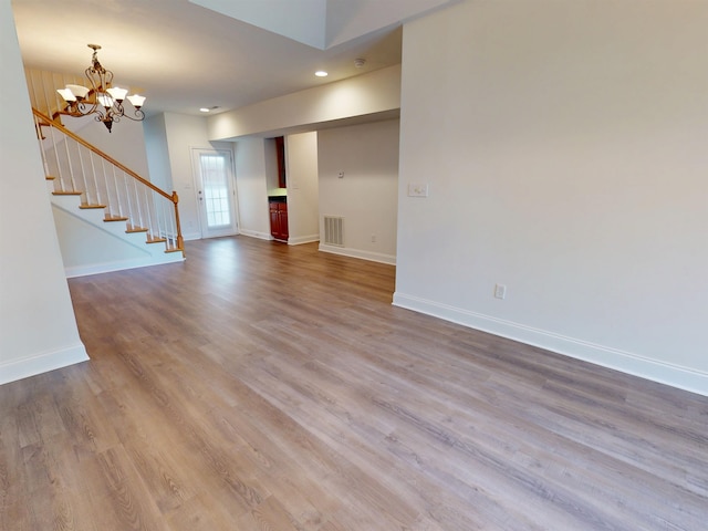unfurnished living room with baseboards, a chandelier, wood finished floors, and visible vents
