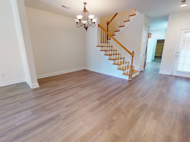 unfurnished dining area featuring a notable chandelier, wood finished floors, and stairway