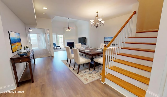dining room featuring a fireplace, ceiling fan with notable chandelier, stairs, and wood finished floors