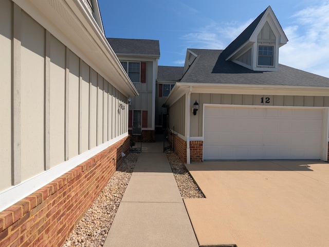 view of property exterior featuring a shingled roof, board and batten siding, concrete driveway, and brick siding
