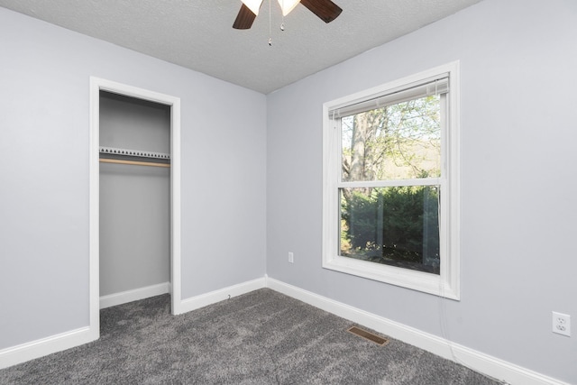unfurnished bedroom featuring baseboards, dark colored carpet, a textured ceiling, and visible vents