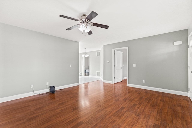 spare room with ceiling fan with notable chandelier, wood finished floors, visible vents, and baseboards