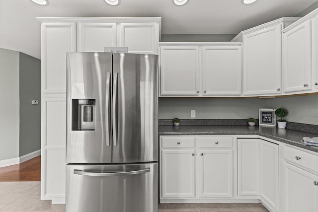 kitchen with dark countertops, stainless steel fridge, and white cabinetry