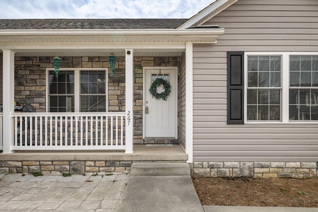 view of exterior entry with covered porch and roof with shingles