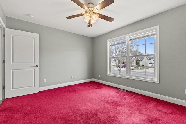 unfurnished room with a ceiling fan, dark colored carpet, visible vents, and baseboards