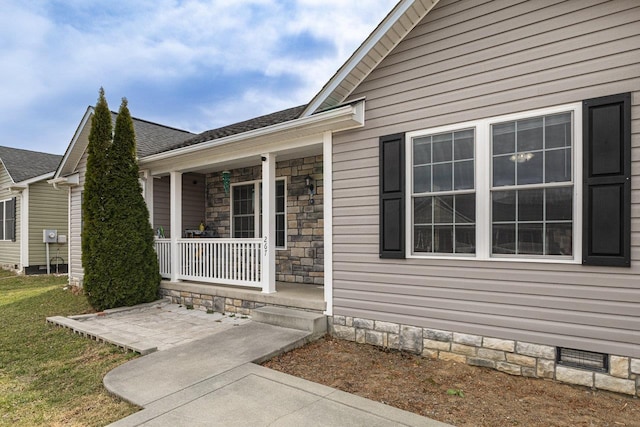 property entrance with a yard, a shingled roof, covered porch, crawl space, and stone siding