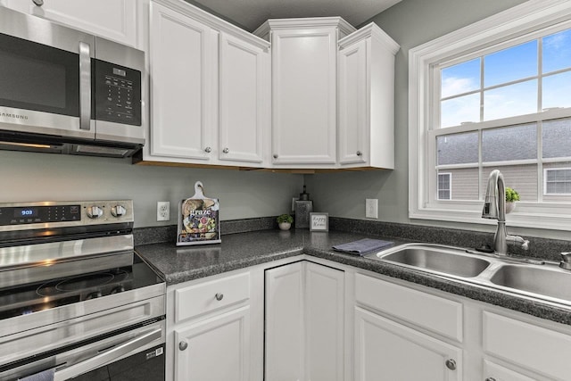 kitchen with white cabinets, dark countertops, stainless steel appliances, and a sink