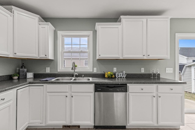 kitchen featuring stainless steel dishwasher, dark countertops, a sink, and white cabinetry