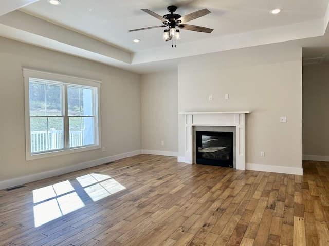 unfurnished living room with a fireplace, a raised ceiling, ceiling fan, and light wood-type flooring