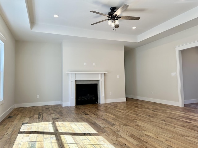 unfurnished living room with a raised ceiling, ceiling fan, and light wood-type flooring