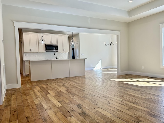 kitchen with pendant lighting, white cabinetry, a kitchen island with sink, and light wood-type flooring