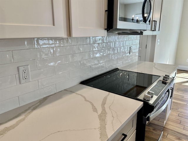 kitchen with light stone counters, white cabinetry, light hardwood / wood-style floors, and range with electric cooktop