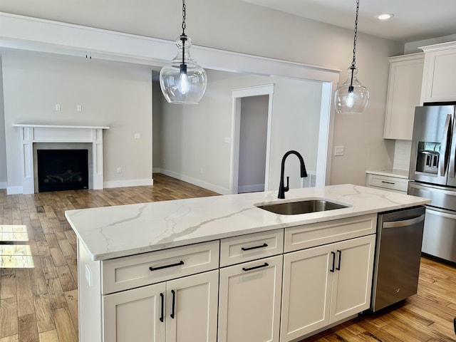 kitchen featuring appliances with stainless steel finishes, an island with sink, sink, light stone counters, and light hardwood / wood-style floors