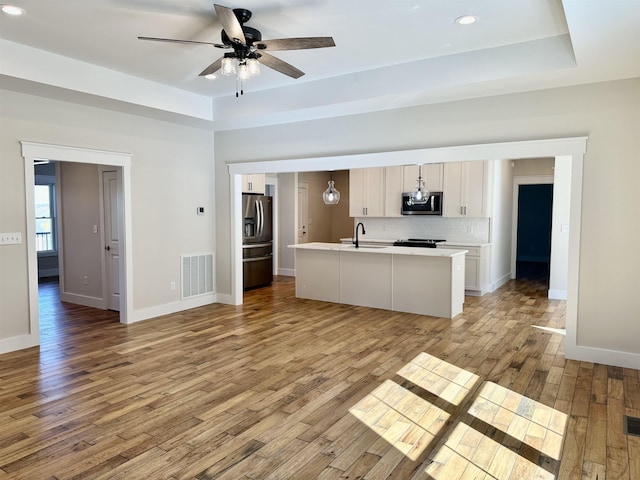 kitchen featuring sink, appliances with stainless steel finishes, white cabinetry, an island with sink, and decorative light fixtures