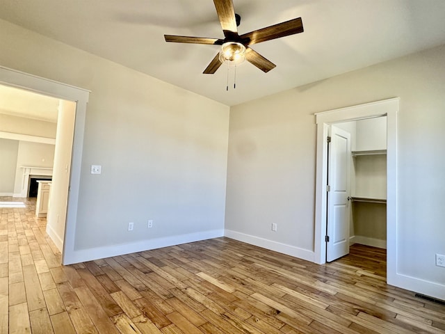 unfurnished bedroom with ceiling fan, a walk in closet, a closet, and light wood-type flooring