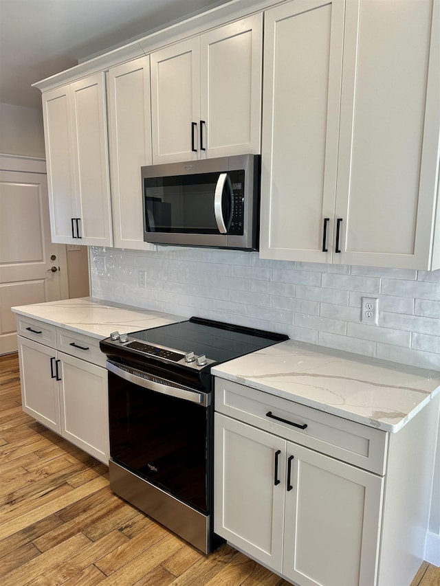 kitchen with light stone counters, stainless steel appliances, white cabinets, and light wood-type flooring