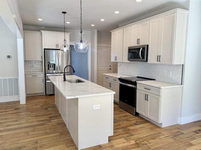 kitchen with appliances with stainless steel finishes, white cabinetry, a center island with sink, decorative light fixtures, and light wood-type flooring