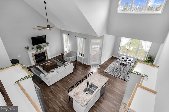 living area with a fireplace with flush hearth, high vaulted ceiling, dark wood-style floors, baseboards, and ceiling fan