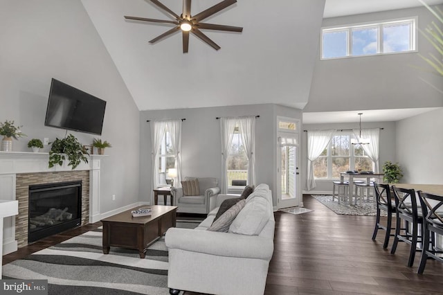 living room featuring baseboards, a glass covered fireplace, dark wood-style flooring, and ceiling fan with notable chandelier