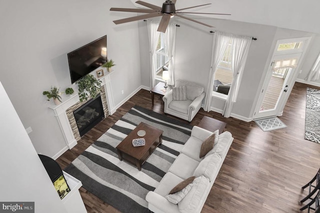 living area featuring a glass covered fireplace, wood finished floors, baseboards, and ceiling fan