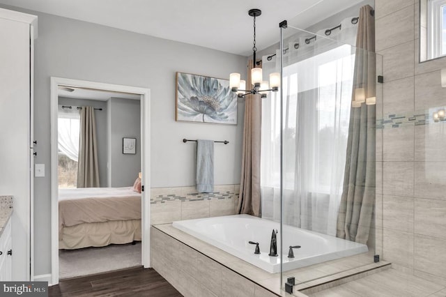 bathroom with wood finished floors, ensuite bath, a shower stall, tiled tub, and a chandelier