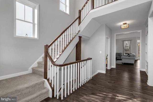 stairway featuring baseboards, wood finished floors, and a towering ceiling