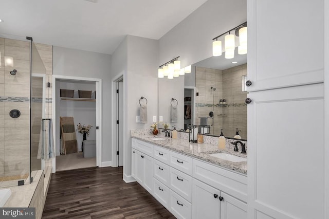 bathroom featuring double vanity, wood finished floors, a stall shower, and a sink