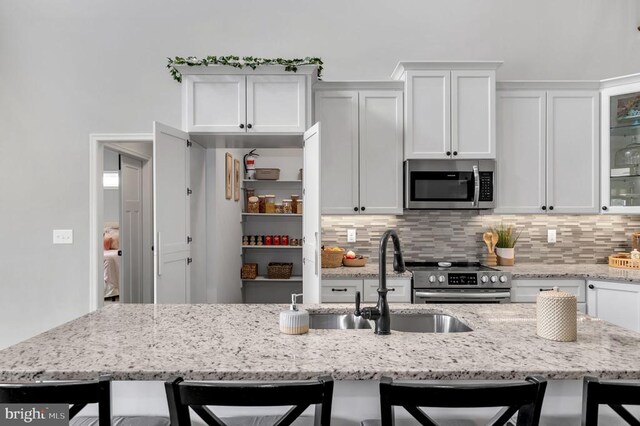 kitchen with a sink, a kitchen breakfast bar, appliances with stainless steel finishes, white cabinets, and decorative backsplash