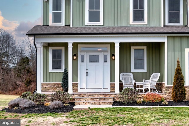 view of exterior entry featuring board and batten siding, covered porch, stone siding, and a shingled roof