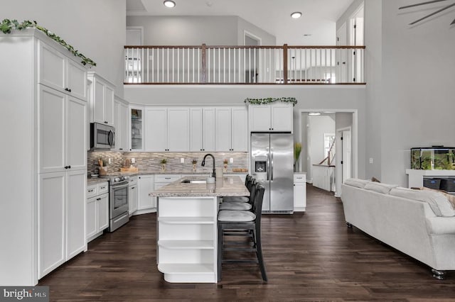 kitchen featuring a high ceiling, a sink, stainless steel appliances, dark wood-type flooring, and white cabinetry