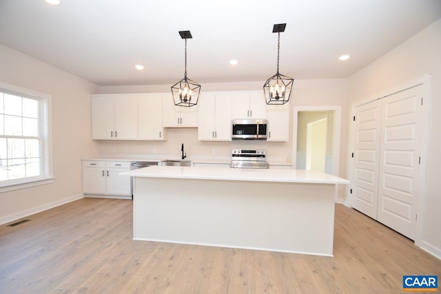 kitchen featuring appliances with stainless steel finishes, hanging light fixtures, a kitchen island, and white cabinets