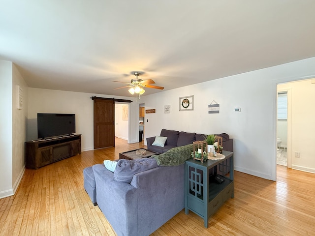 living room with ceiling fan, a barn door, and light hardwood / wood-style floors