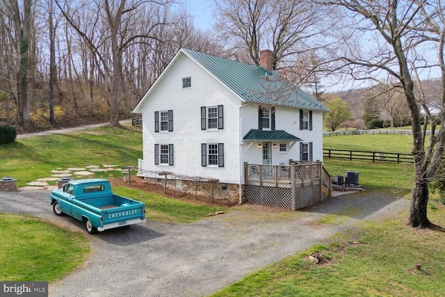 view of front of home featuring metal roof, driveway, crawl space, a standing seam roof, and a chimney