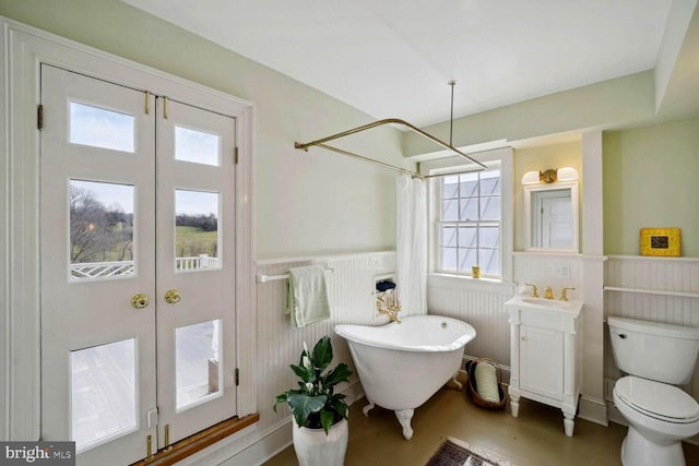 bathroom with a wainscoted wall, curtained shower, toilet, vanity, and a freestanding tub