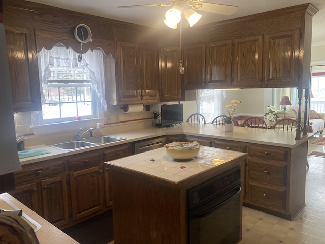 kitchen with a peninsula, a sink, black oven, a center island, and light floors