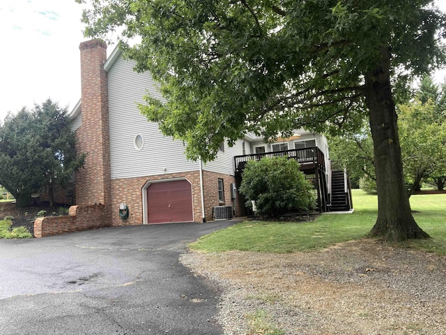 view of property exterior with a deck, brick siding, driveway, stairway, and a chimney