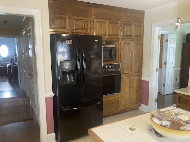 kitchen with black appliances, ornamental molding, brown cabinetry, and hanging light fixtures