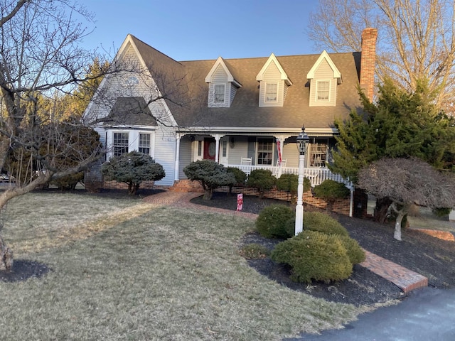 view of front of house with covered porch, a chimney, and a front lawn