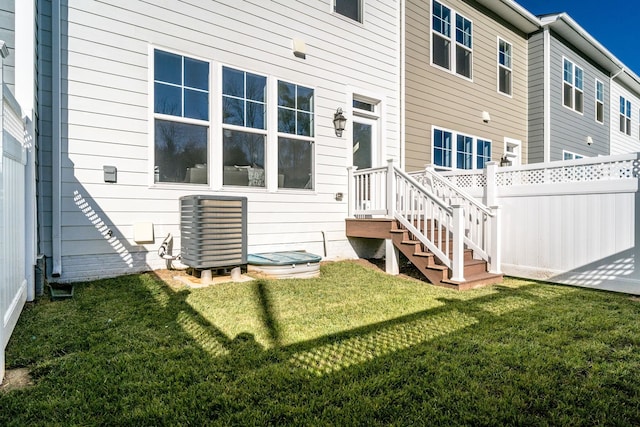 rear view of property featuring central air condition unit and a lawn