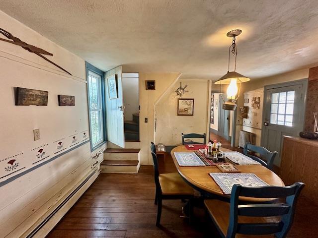 dining area featuring baseboard heating, radiator, dark wood-type flooring, and a textured ceiling