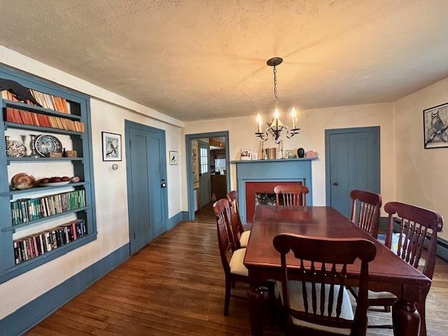 dining area featuring dark wood-type flooring, built in features, an inviting chandelier, and a textured ceiling